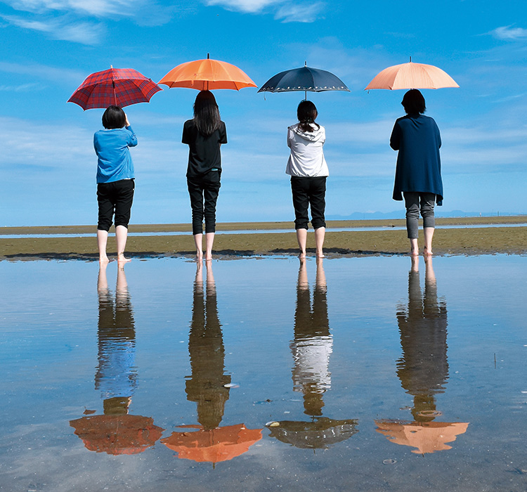 傘を持った４人とその姿が干潟に反射している写真