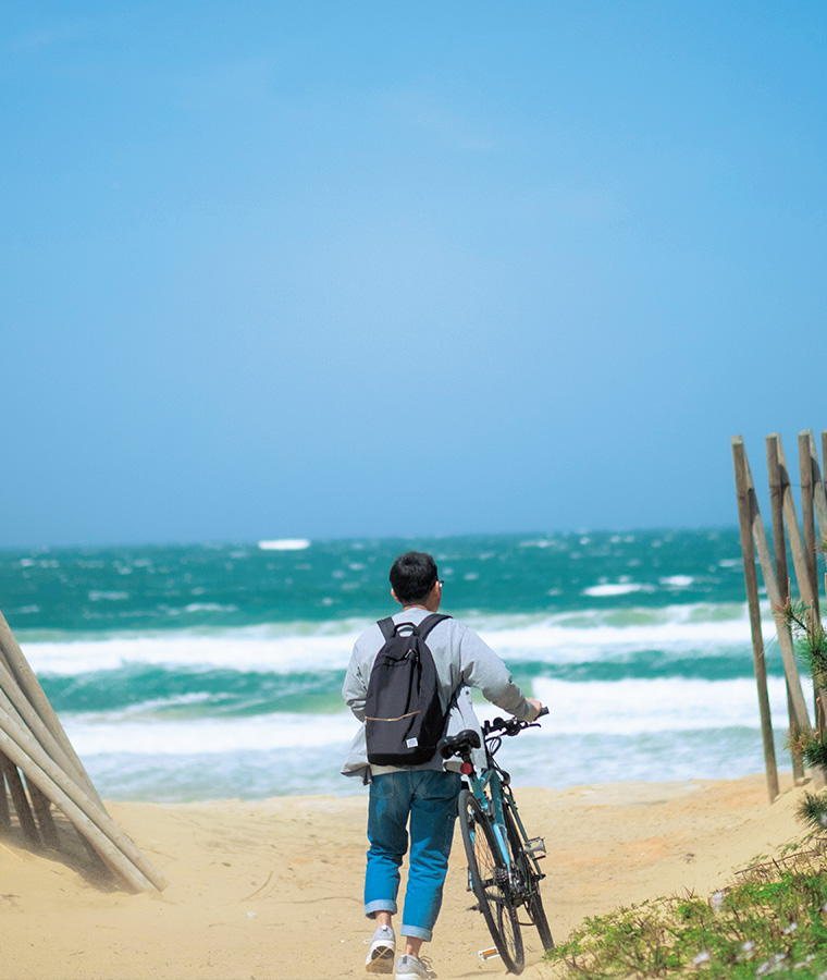砂浜で自転車を押す男性の後ろ姿の写真