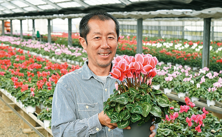 シクラメンの鉢花を持ち笑顔の西岡宏祐さんの写真