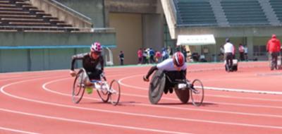 陸上競技場でレース用車いすをこぐ２名の選手の画像