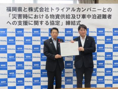 服部知事と濱崎福岡支社長が協定書を掲げるようす