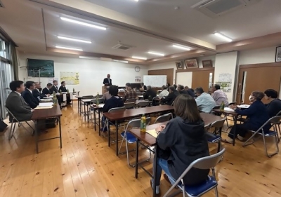 総会のようすの写真。発起人代表があいさつをしているのを、多くの会員が席に座って聞いている。