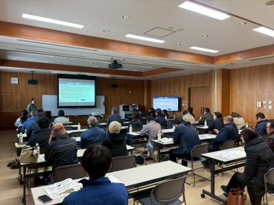 講師が聴衆に対してスライドを用いて説明している様子