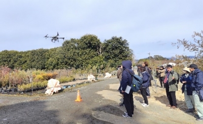 植木ほ場の上を飛行するドローン防除機とそれを見る参加者達